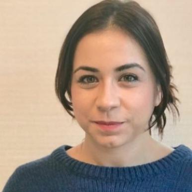 Woman with her hair pulled back, in blue sweater, looks into the camera