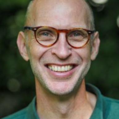 Caucasian man without hair, wearing red glasses and a green polo shirt, smiles into the camera