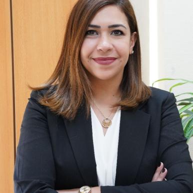 Woman with light brown hair, in a black blazer, crosses her arms and smiles into the camera 