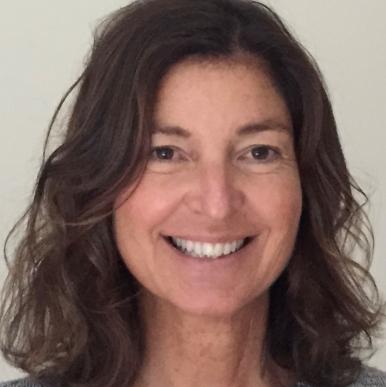 Woman with brown hair to her shoulders, wearing a gray sweater, smiles into the camera