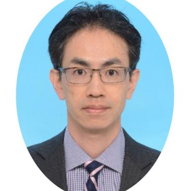 Man with short brown hair wearing glasses, with a suit jacket and tie, stands in front of a light blue background