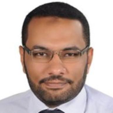 Man with short dark hair and a short beard, wearing glasses, looks into the camera