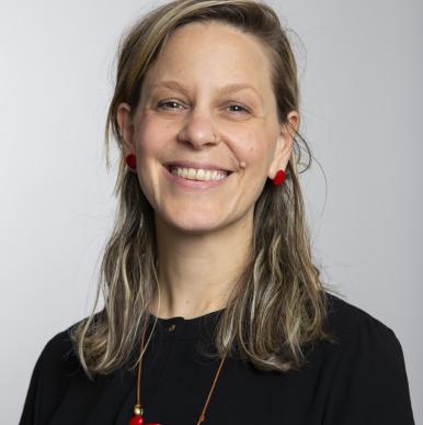 Emily Tagliaro headshot Woman wearing a black shirt and red necklace smile into the camera
