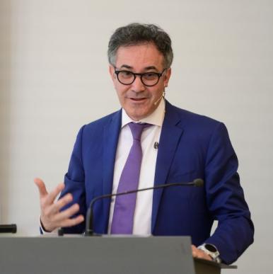 Man wearing a blur suit and glasses stands at a podium