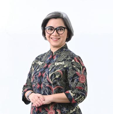 Photo of woman wearing patterned shirt and round glasses, smiles into camera