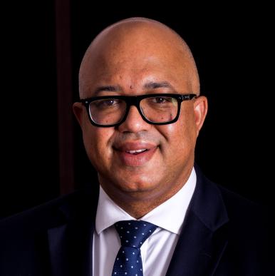 Man wearing glasses, wearing a black suit and blue tie, stand in front of a black background