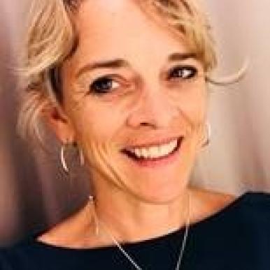 Woman with blonde hair, wearing hoop earrings and a black shirt, smiles into the camera