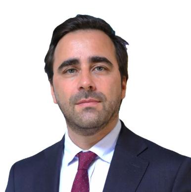 Man with brown hair looks into the camera, wearing a blue suit with a white undershirt
