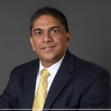 Man wearing a black suit with a yellow tie looks into the camera