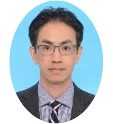 Man with short brown hair wearing glasses, with a suit jacket and tie, stands in front of a light blue background