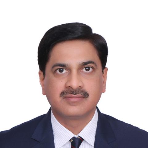 Man wearing a blue suit, with a brown moustache, looks into the camera