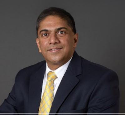 Man wearing a black suit with a yellow tie looks into the camera