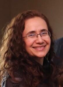 Woman with brown curly hair and glasses smiles into the camera