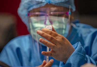 Person in blue medical scubs draws a vaccine from a vile into a syringe