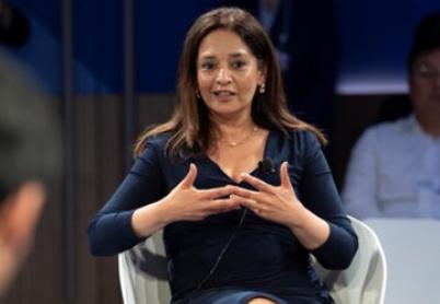 Priya Basu sits in a white chair, wearing a blue dress