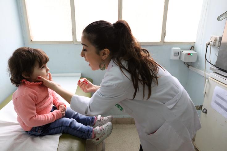 Lebanon nurse vaccinates child for polio Nurse wearing a white bends down to a child and makes the motion to open their mouth, with a liquid dropper in one hand